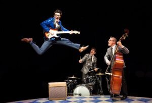 Kieran McCabe jumping off the ground, Jed Feder on drums, and Shaun Whitley on bass In The Buddy Holly Story at Marriott Lincolnshire